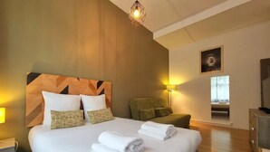 A hotel room with a large bed, a green armchair, a desk, and a lamp.