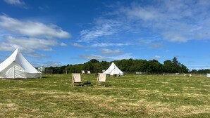 Un terrain de camping avec des tentes et des chaises, situé dans un champ herbeux.