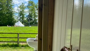 Un porte-rouleau de papier toilette fixé à une porte blanche, avec vue sur un champ verdoyant et une clôture blanche.