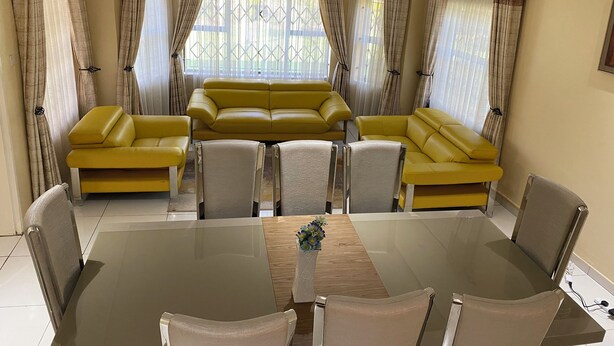 Een woonkamer met een geel sofa-ensemble, een glazen eettafel en een decoratieve vaas.
