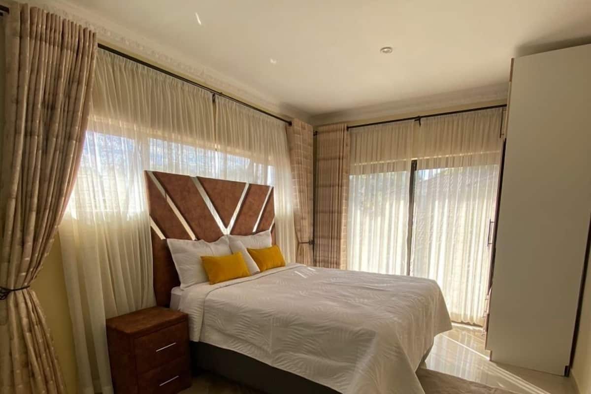Een slaapkamer met een bed, nachtkastjes, een houten hoofdbord en dunne gordijnen.