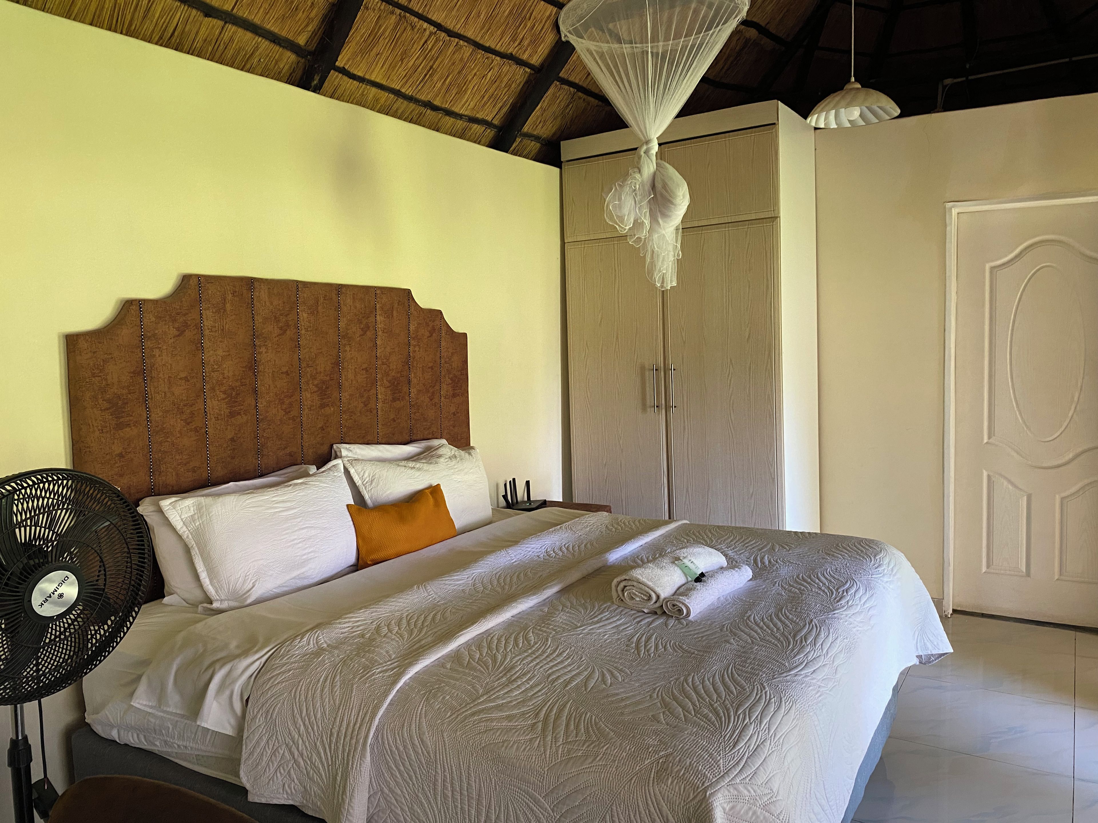 A neatly made bed with a headboard, a bedside fan, and a wardrobe with a door.
