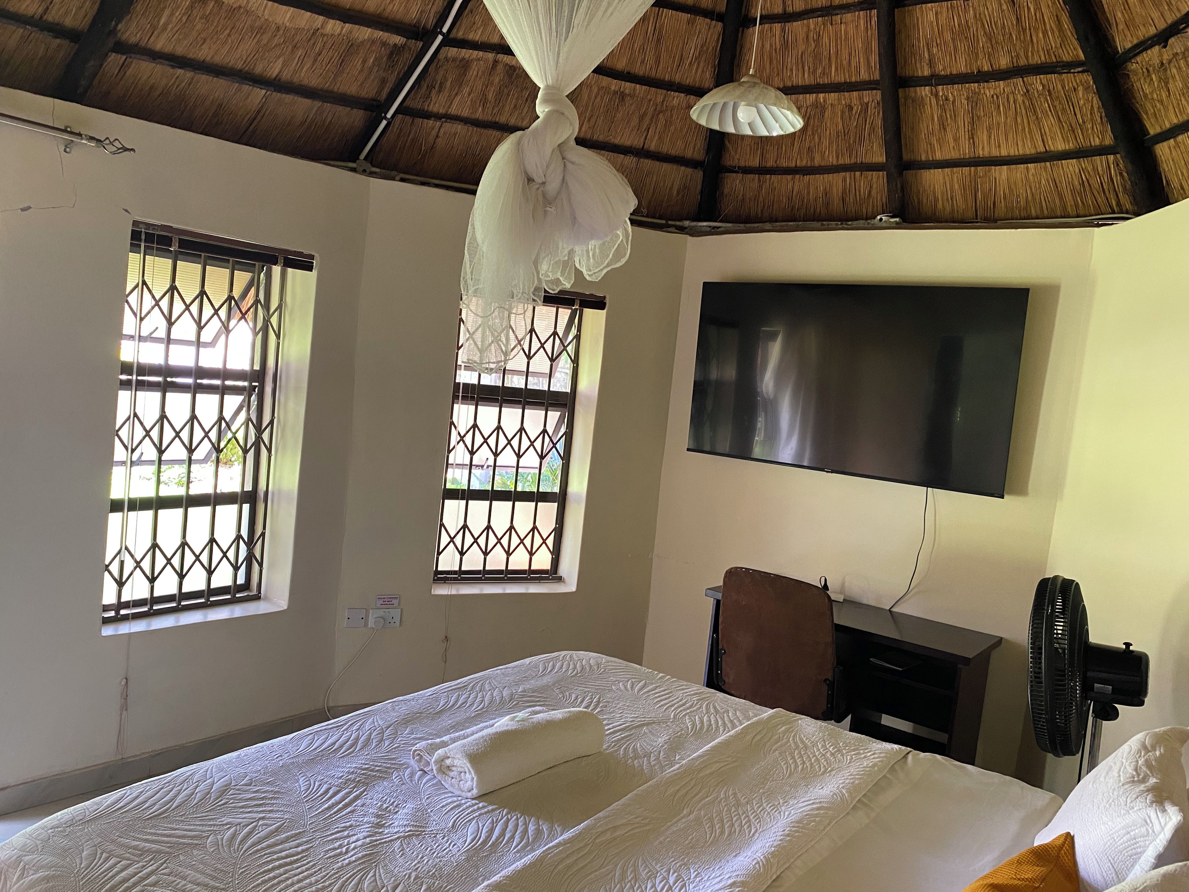 Ein Hotelzimmer mit einem Bett, einem Fernseher, einem Schreibtisch und einem Ventilator.