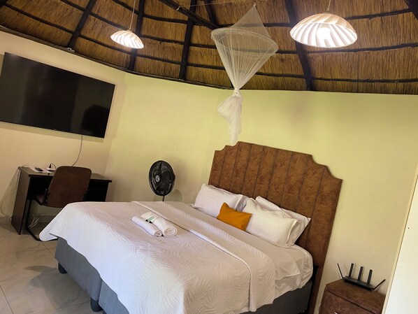 A hotel room with a bed, a desk, a chair, a fan, and a ceiling fan.