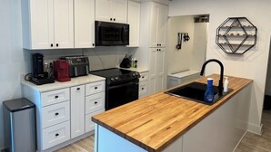 Een moderne keuken met witte kasten, een houten aanrecht, een zwarte kookplaat en een magnetron.