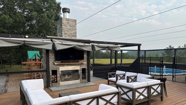 Een terras buiten met een stenen open haard, witte zachte zitplaatsen en een zwembad op de achtergrond.