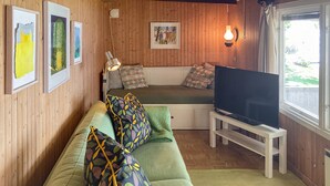 A cozy room with a green sofa, a flat-screen TV on a stand, wooden walls, and framed pictures. - Beautiful home in Tranås with lake view (Tranås)