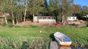 A small cabin with a porch, surrounded by trees and a grassy area with a dock and a boat. - Beautiful home in Tranås with lake view (Tranås)