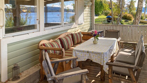 A covered outdoor seating area with a bench, table, and chairs, overlooking a lake and garden. - Beautiful home in Tranås with lake view (Tranås)