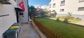 A courtyard with a green lawn, a wooden fence, and a flag. - Diana's Suites Ephesus (Selçuk)