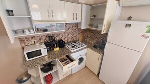 A compact kitchen with a microwave, gas stove, sink, and a washing machine. - Diana's Suites Ephesus (Selçuk)