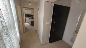 A hallway with a dark door, a light switch, and a visible kitchen area in the background. - Diana's Suites Ephesus (Selçuk)
