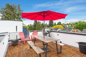 A rooftop terrace with a wooden deck, a red umbrella, two red chairs, a table, and a potted plant. - Stylish Townhouse Near Seattle Attractions with EV Charger (Seattle)