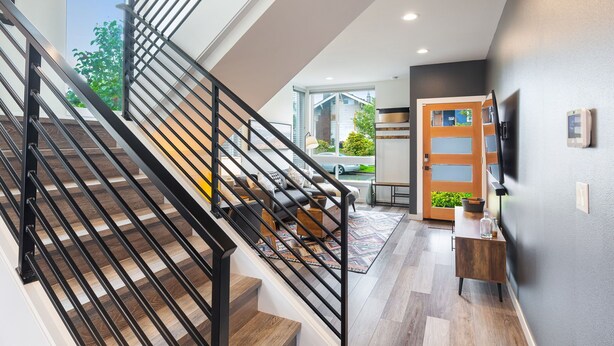 A modern staircase with black railings, leading to a living area with a sofa, coffee table, and a view of the outdoors.