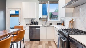 A modern kitchen with white cabinets, a stainless steel dishwasher, a gas stove, and a window with a view of the outside.
