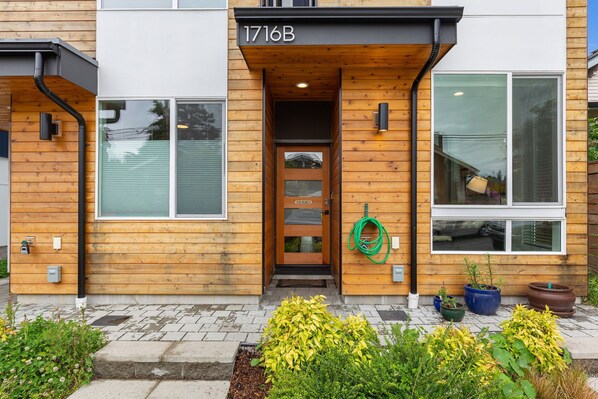 A modern building with a wooden facade, a glass door entrance, and a number plate '1716B'. - Stylish Townhouse Near Seattle Attractions with EV Charger (Seattle)