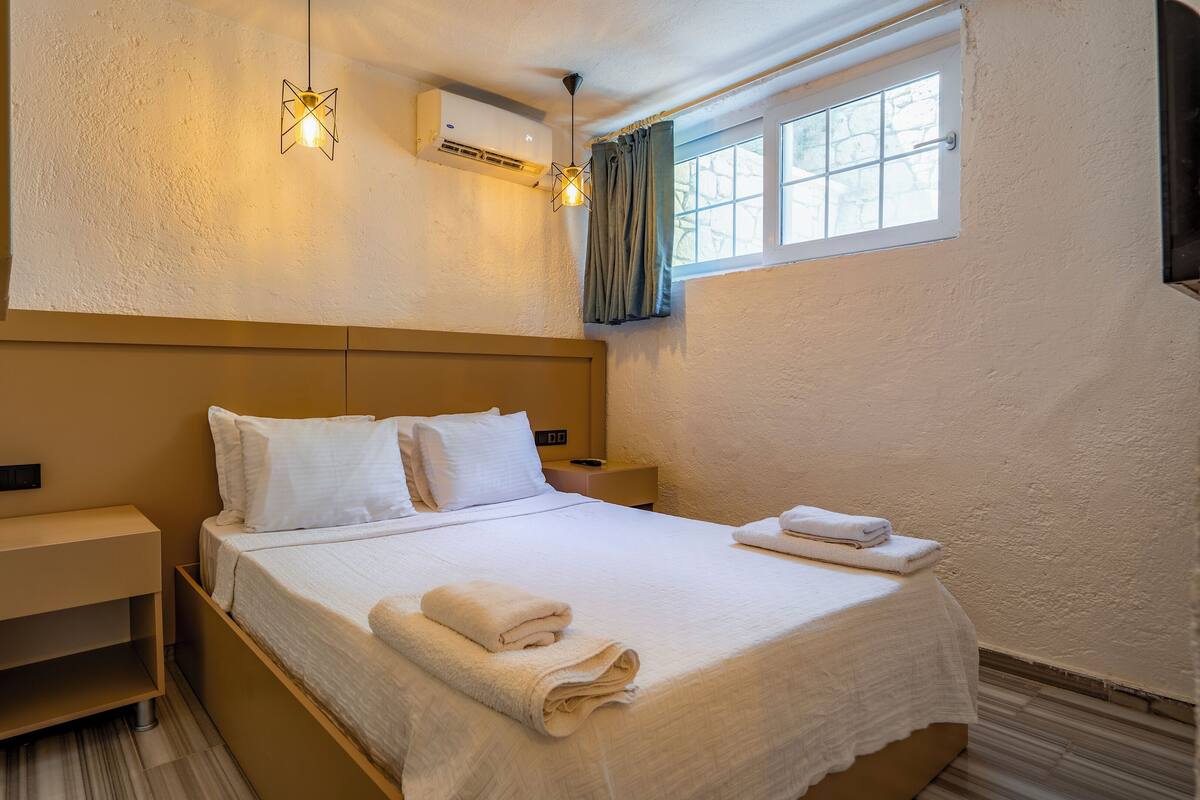 Une chambre d’hôtel avec un lit, des tables de chevet, un climatiseur fixé au mur et une fenêtre avec des rideaux.
