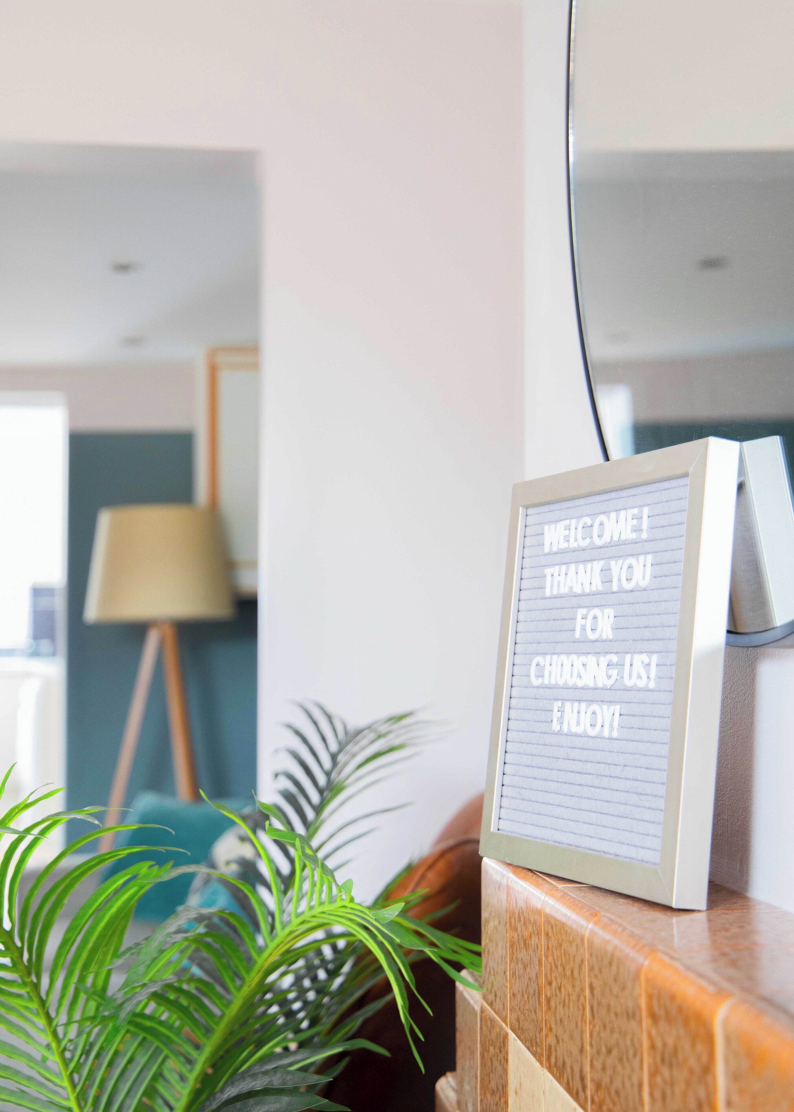 A welcome sign with a thank you message, a lamp, and a plant in a room.
