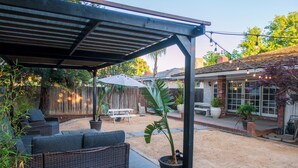 A covered patio with wicker furniture, a potted plant, and string lights. - Modern home 3-BR Retreat — Quiet, Cozy, & Family-Friendly in Fresno. (Fresno)