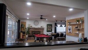 A room with a pool table, a fireplace, and a clock on the wall. - Modern home 3-BR Retreat — Quiet, Cozy, & Family-Friendly in Fresno. (Fresno)