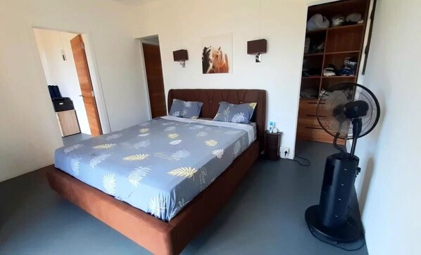 A bedroom with a bed, a fan, and a wardrobe.