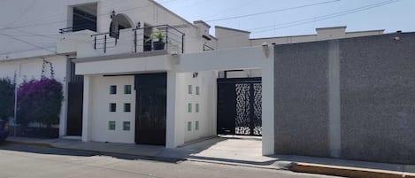 A modern two-story house with a balcony, a garage, and a gated entrance.