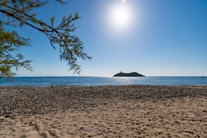 Une plage de galets avec une petite île qui se profile à l’horizon.