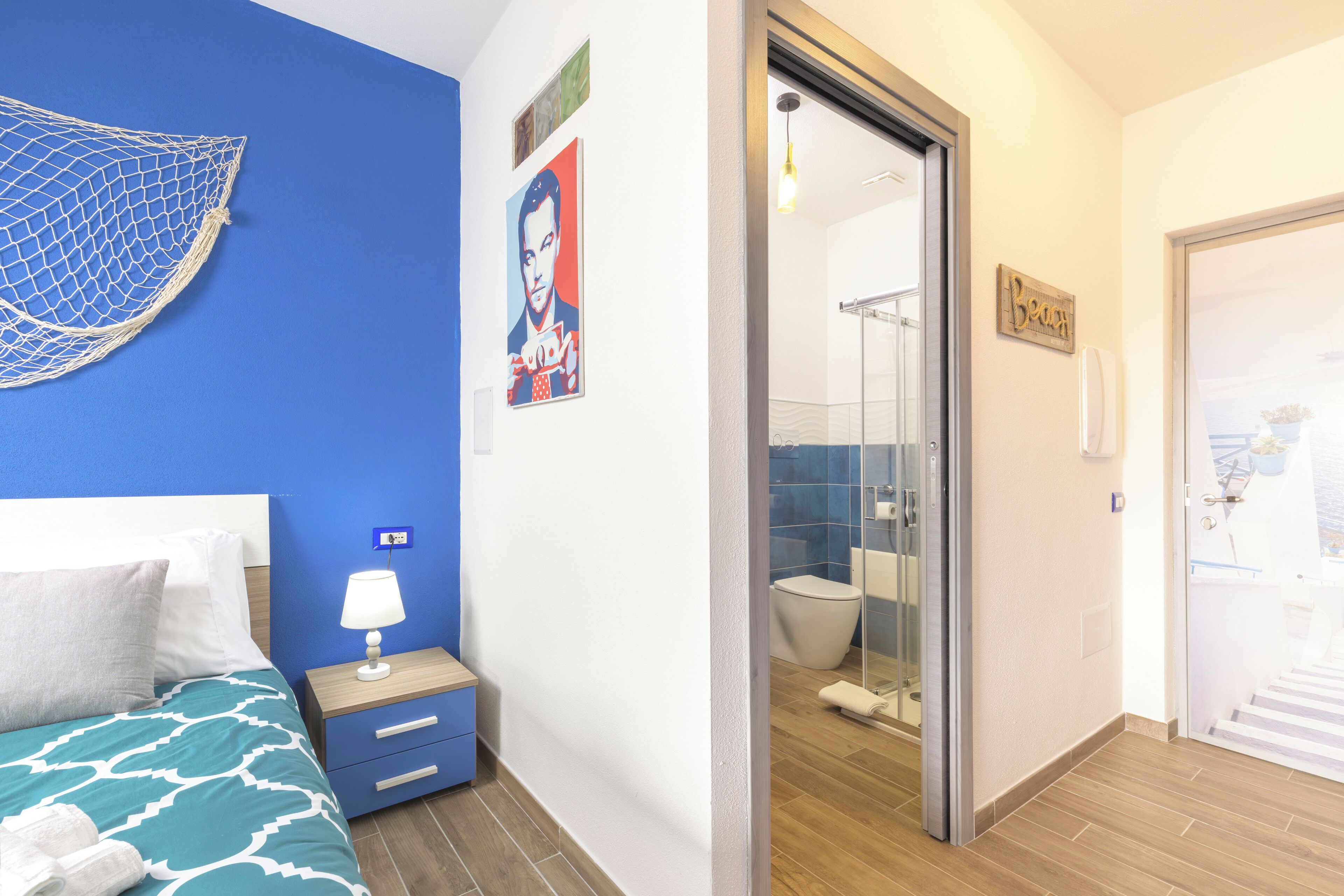 Habitación de hotel con cama, mesita de noche, baño con ducha y puerta que da a un balcón.