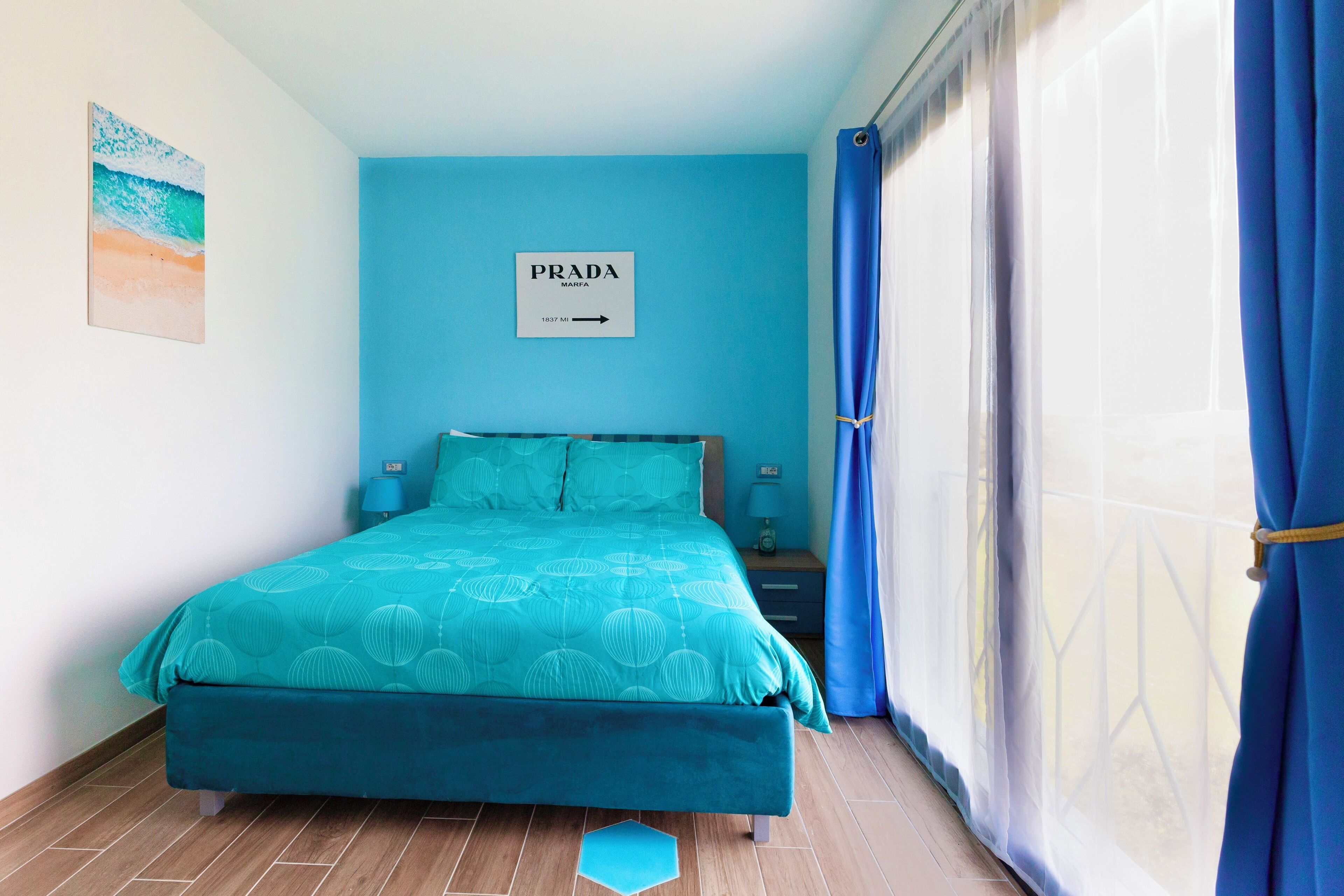 A bedroom with a bed, a sign on the wall, a nightstand, and a window with curtains.
