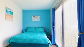 A bedroom with a bed, a sign on the wall, a nightstand, and a window with curtains.