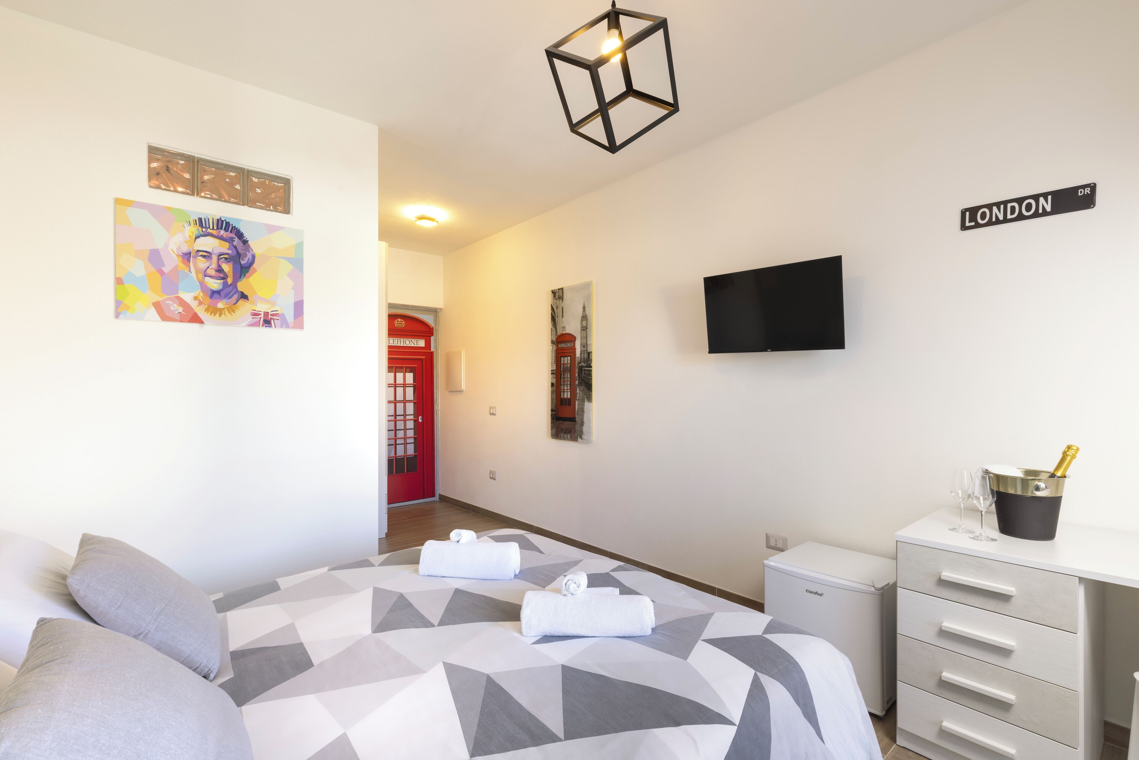 A hotel room with a bed, a desk, a television, and a wall with a London sign.