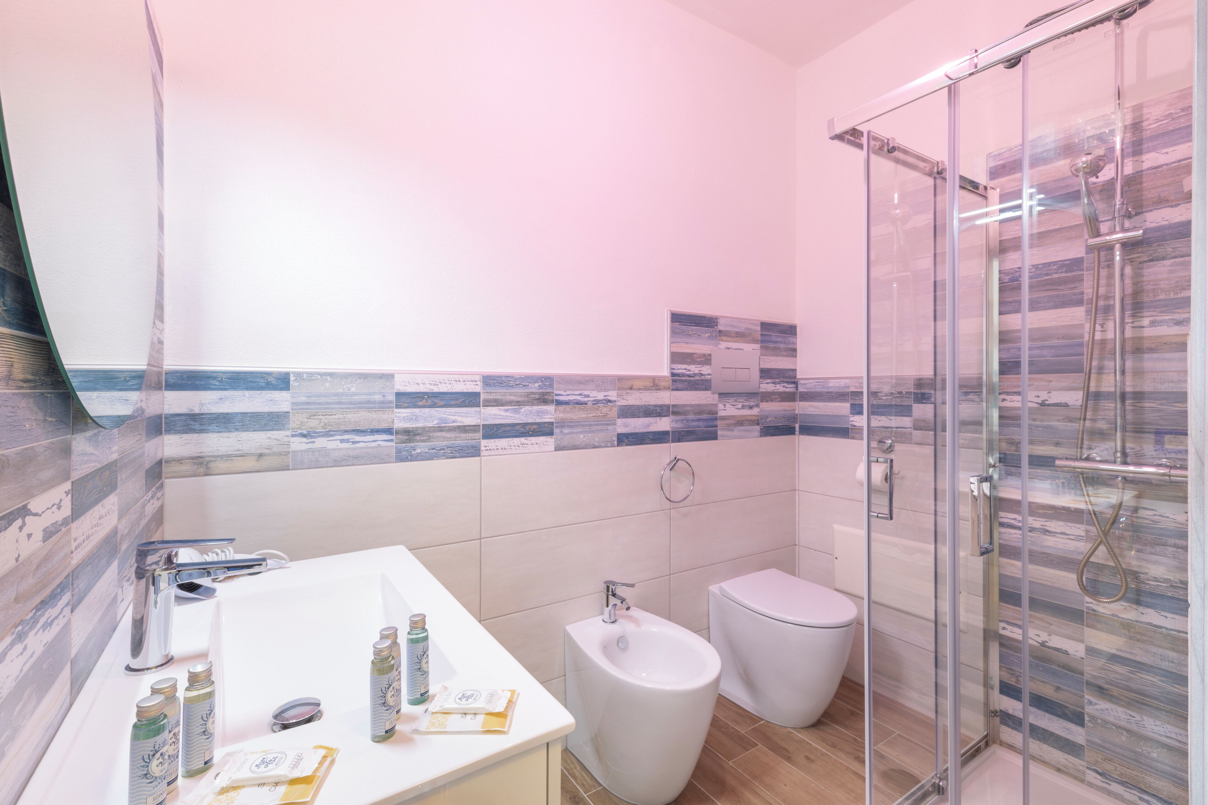 A bathroom with a glass shower enclosure, a bidet, and a white sink with toiletries.