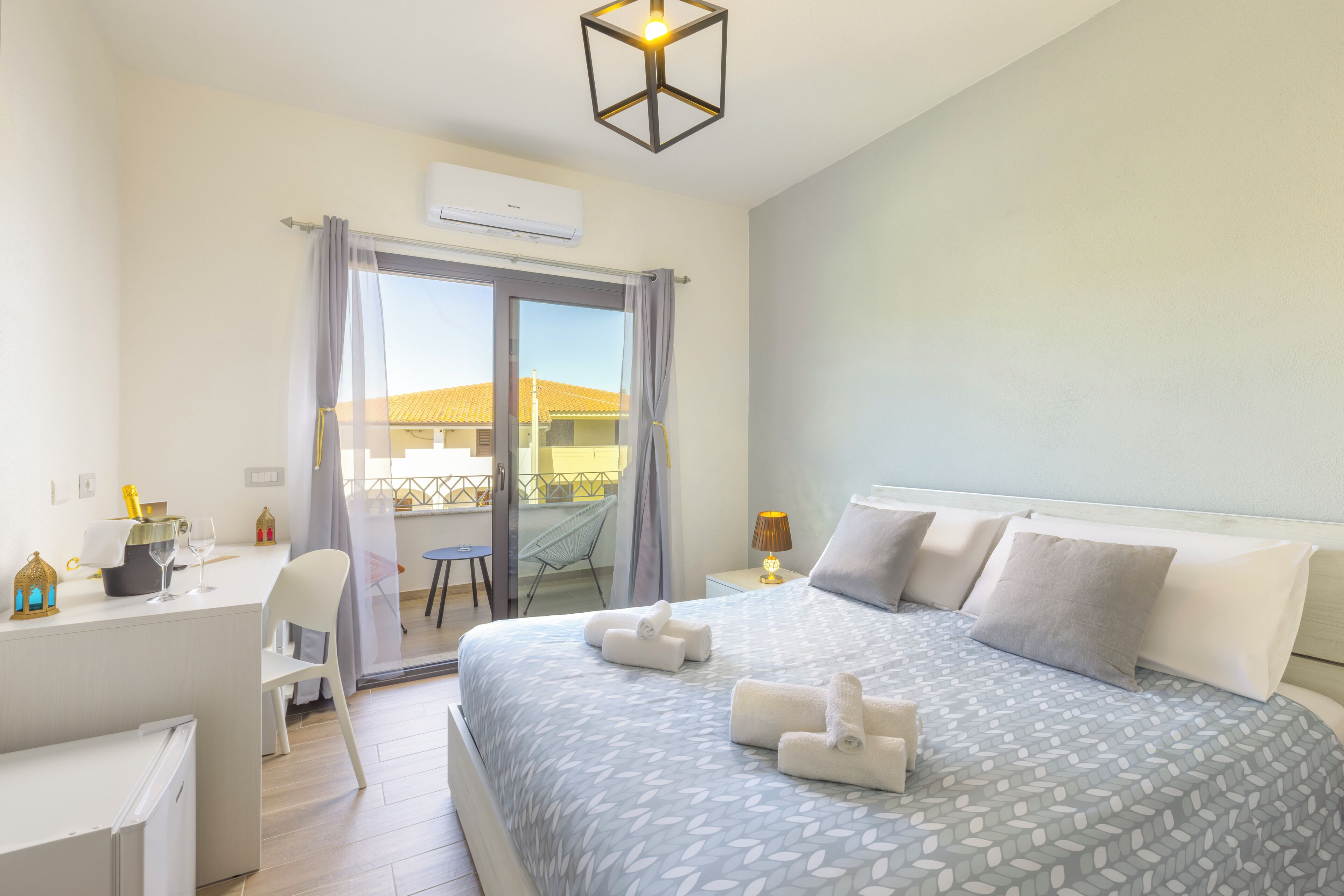 A hotel room with a bed, a desk, a chair, a lamp, and a view of the outside.