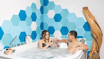 Eine Badewanne mit Wand aus blauen, sechseckigen Fliesen, einer Holzskulptur und einem kleinen Waschbecken mit Pflegeprodukten.