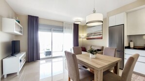 A modern living room with a wooden dining table, comfortable seating, a flat-screen TV, and a large window with curtains. - 1 bedroom beautiful apartment in Cabanes (Cabanes)