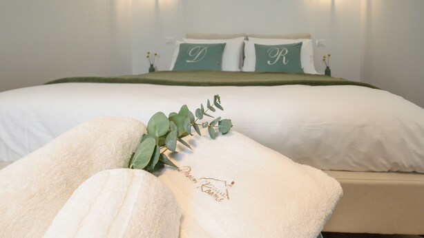 A neatly made bed with white linens, a green throw blanket, and pillows with embroidered initials. - ILLASI DREAM ROOMS (Illasi)