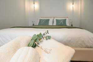 A neatly made bed with white linens, a green throw blanket, and pillows with embroidered initials. - ILLASI DREAM ROOMS (Illasi)
