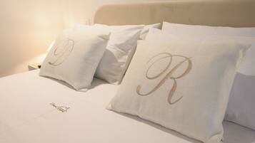 Cama bem arrumada com lençóis e almofadas brancas com iniciais bordadas.