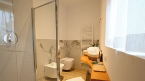 A modern bathroom with a glass shower enclosure, a white toilet, a sink, and a wooden vanity. - ILLASI DREAM ROOMS (Illasi)