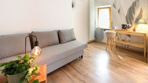 A modern living room with a grey sofa, a wooden coffee table, a potted plant, and a lamp. - ILLASI DREAM ROOMS (Illasi)