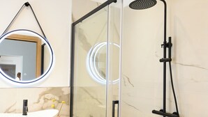 A modern bathroom with a glass-enclosed shower, a white sink, and a wooden vanity. - ILLASI DREAM ROOMS (Illasi)