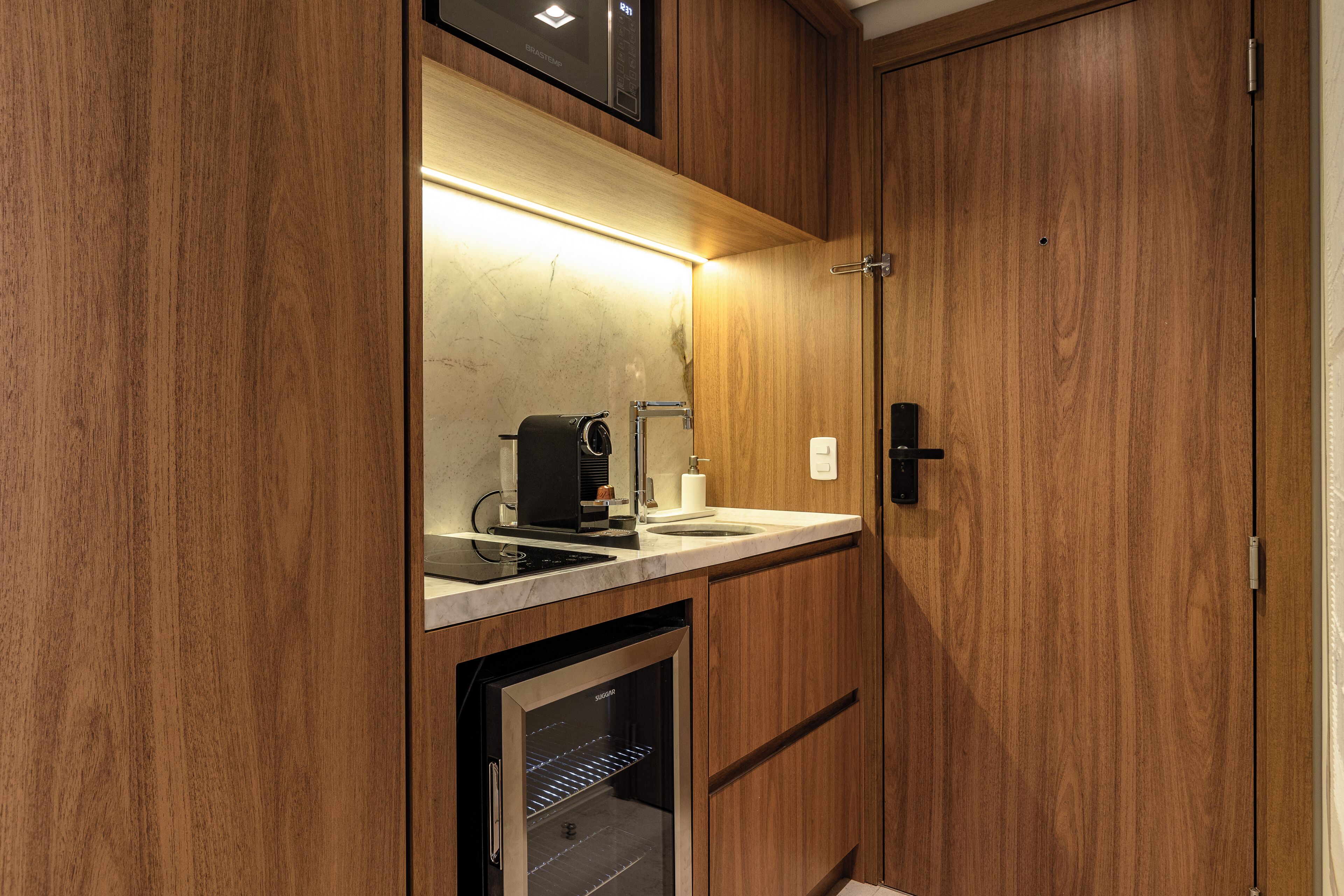 Una cocina compacta con cafetera integrada, un lavamanos y un refrigerador pequeño.