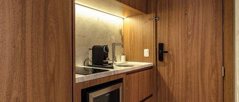 Una cocina compacta con cafetera integrada, un lavamanos y un refrigerador pequeño.