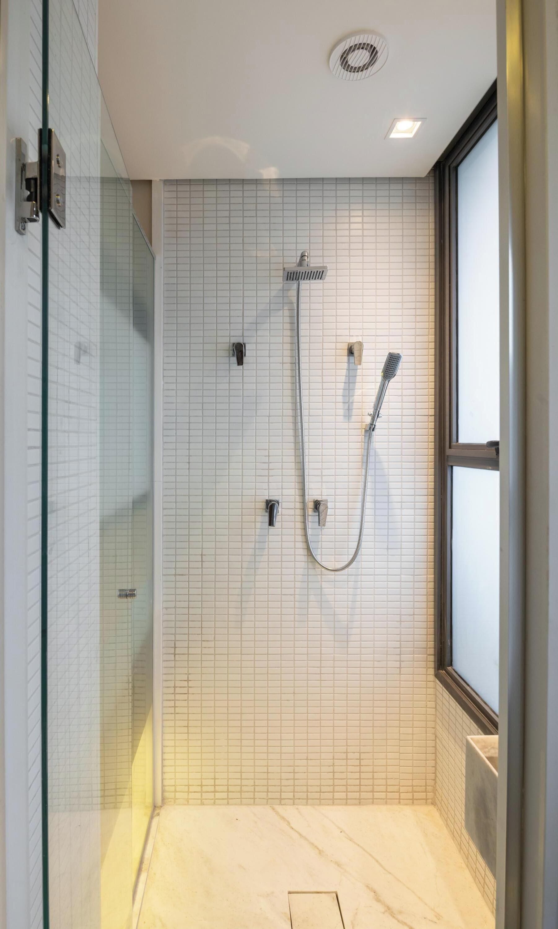 Ein modernes Badezimmer mit Duschkabine aus Glas, einem großen Fenster und Fliesenboden.