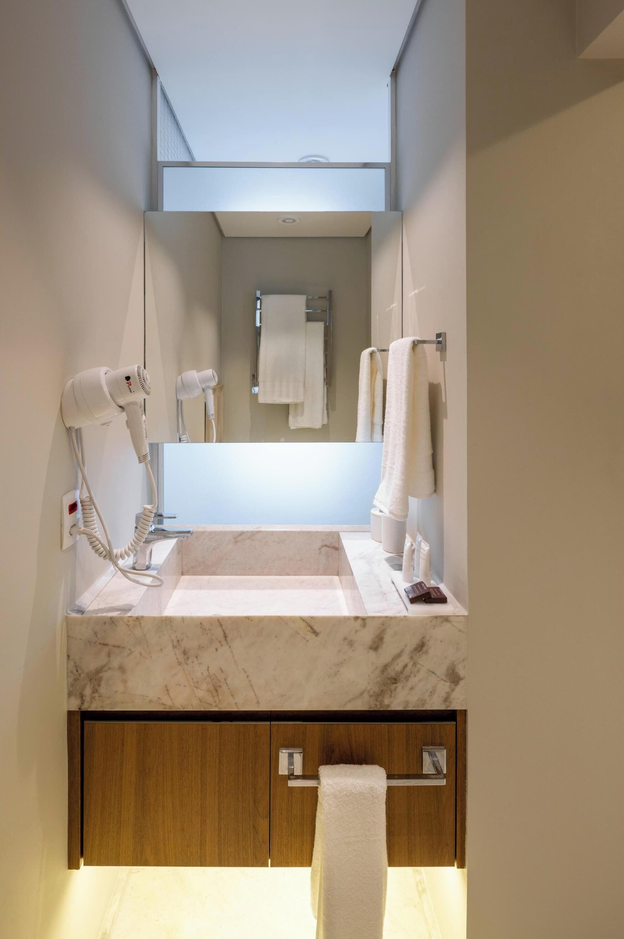 A modern bathroom with a marble sink, built-in hair dryers, a towel rack, and a wooden cabinet.