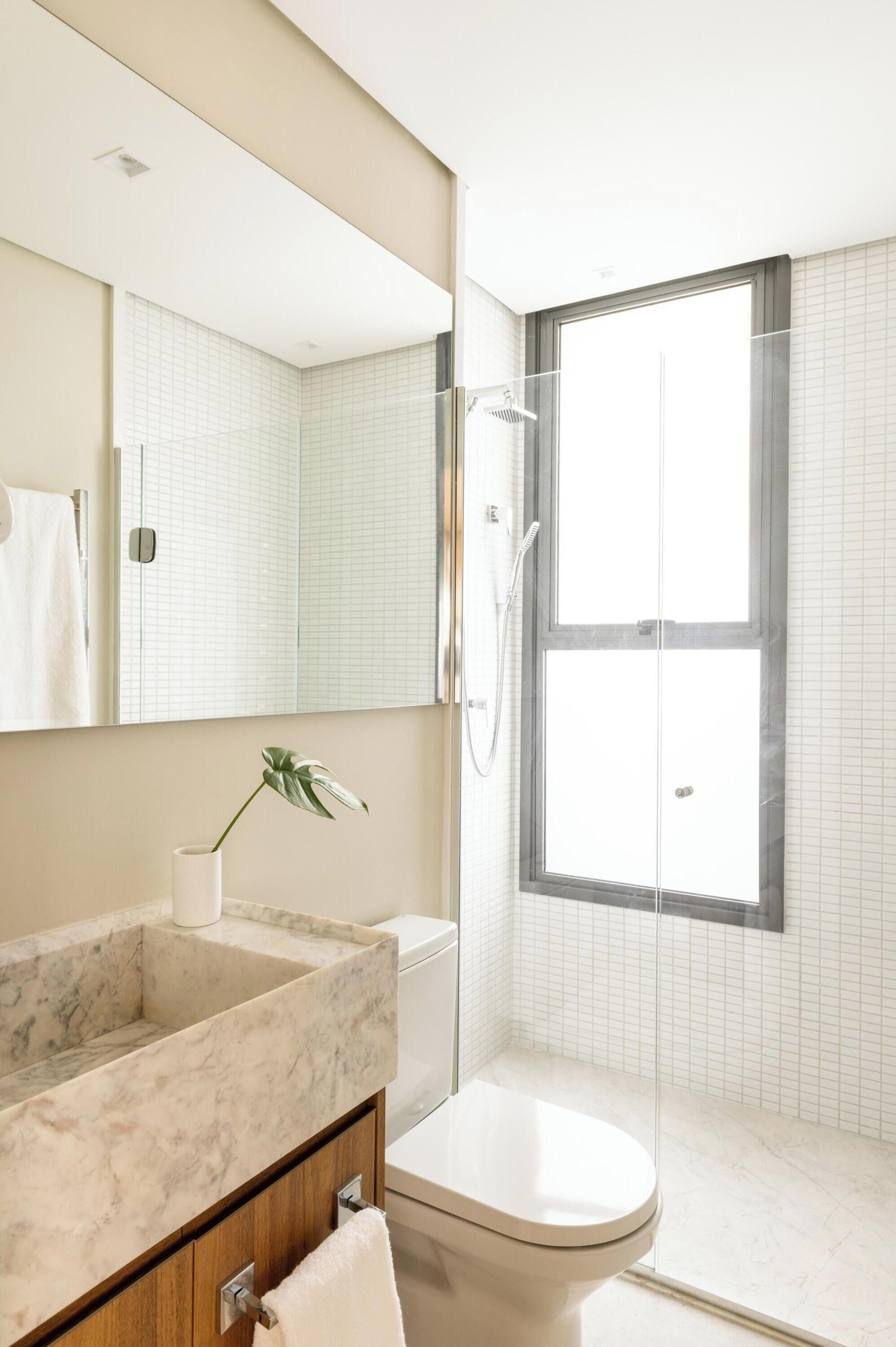 Un baño moderno con lavamanos de mármol, inodoro, cabina de ducha de vidrio y un ventanal amplio.