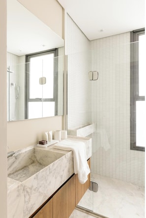 A modern bathroom with a marble sink, wooden cabinets, and a large mirror. - Exclusive Charlie Sintra Jardins (São Paulo)