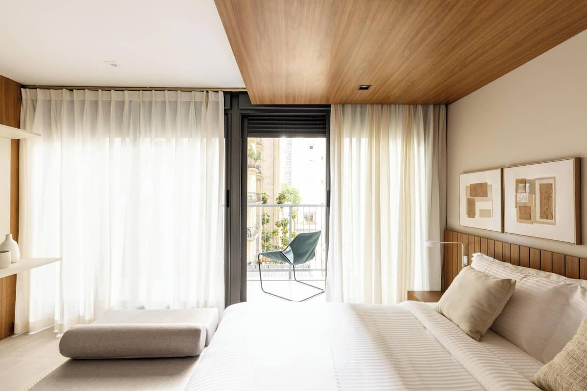 Une chambre d’hôtel moderne avec un grand lit, un balcon avec une chaise et une vue sur la ville.