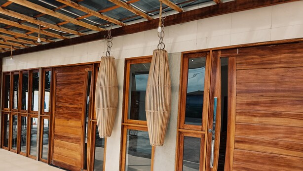 Un bâtiment doté de grandes portes et fenêtres en bois, d’un sol carrelé et d’un plafond avec des poutres en bois et une toiture en métal.