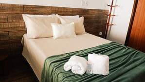 Un lit bien fait, avec une couverture verte et deux serviettes blanches, une tête de lit en bois et un porte-manteau en bois.